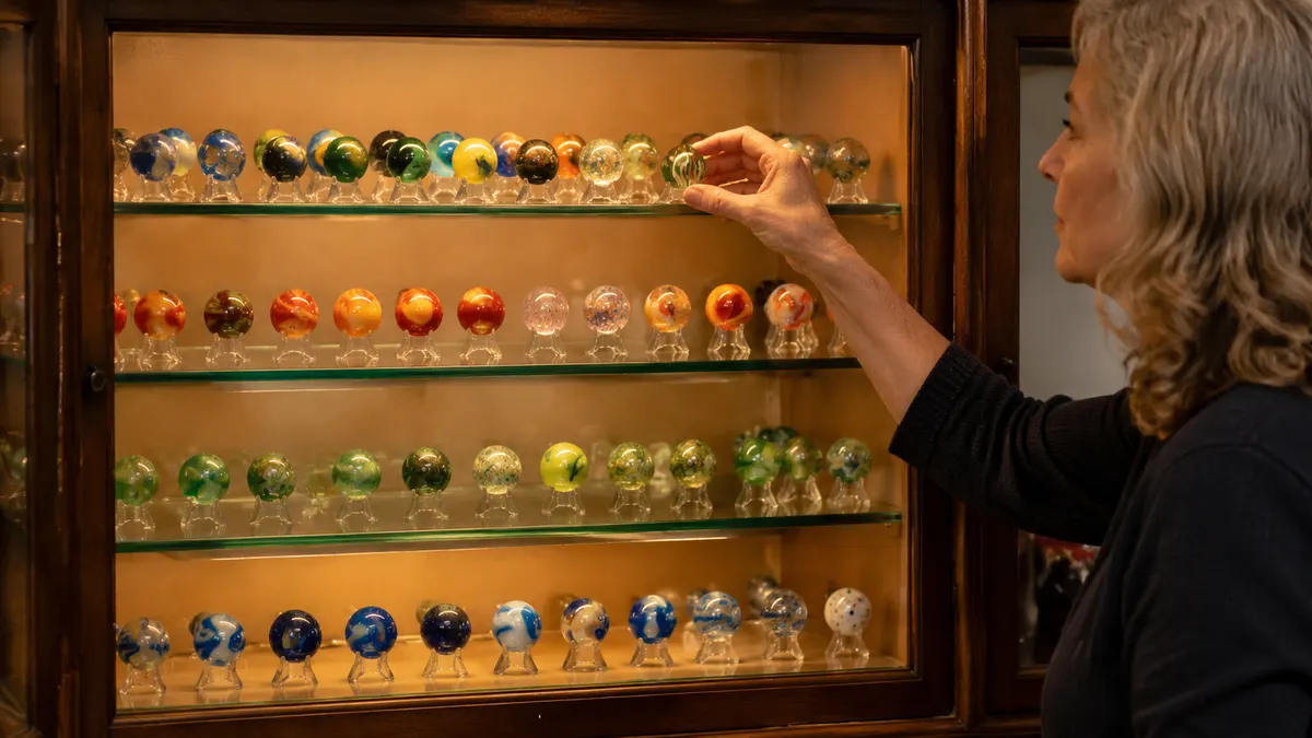 A corner glass display cabinet with rows of marbles on clear acrylic stands, each piece separated and lit