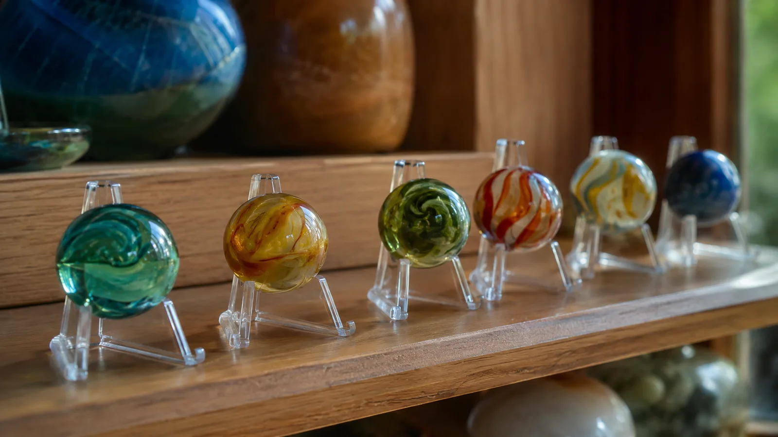 A row of clear acrylic easel stands on a warm pine shelf, each holding a single colored glass marble, soft afternoon light