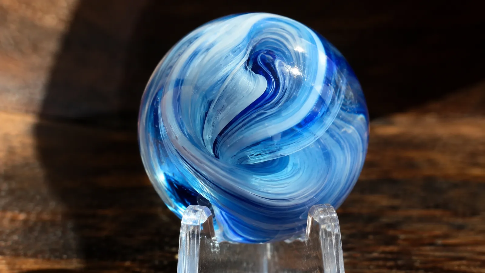 A close-up of a single swirled agate marble resting on a clear easel stand, catching window light through its interior