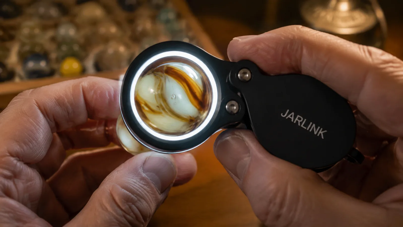 Close shot of the LED-lit loupe lens filling the frame, a marble's swirled glass visible through it