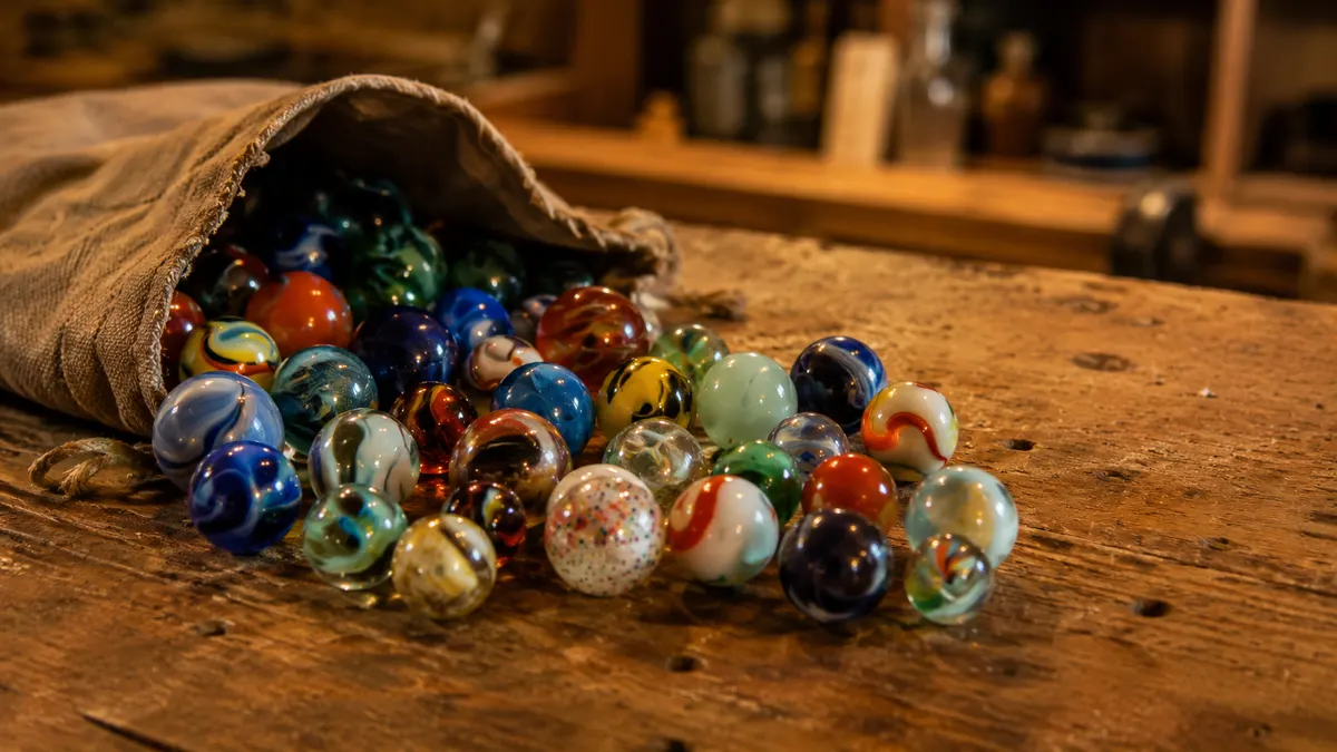 A mixed lot of glass marbles pouring from a cloth pouch onto a worn wood shop bench